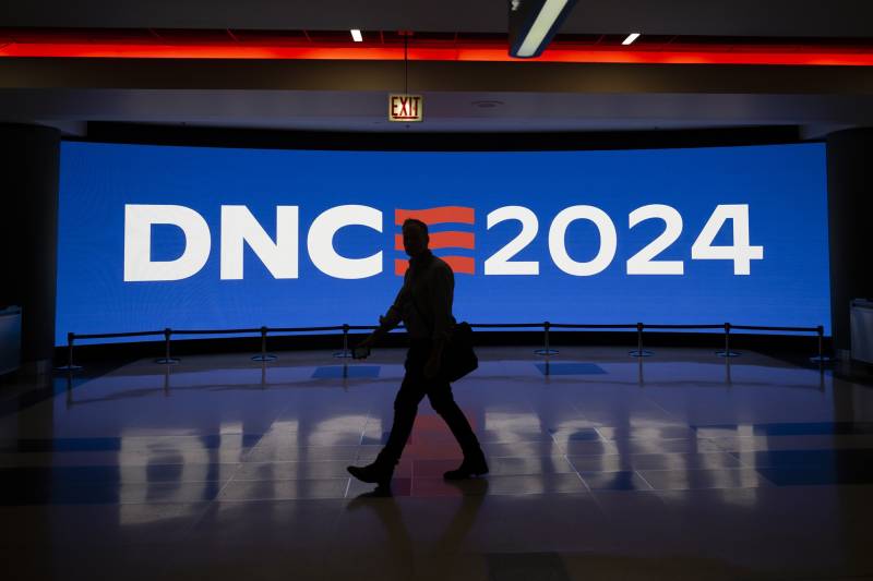 A person walks in front of a digital sign with the DNC 2024 logo