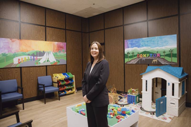 A woman dressed in black clothing stand in a room with a play set and toys behind her.