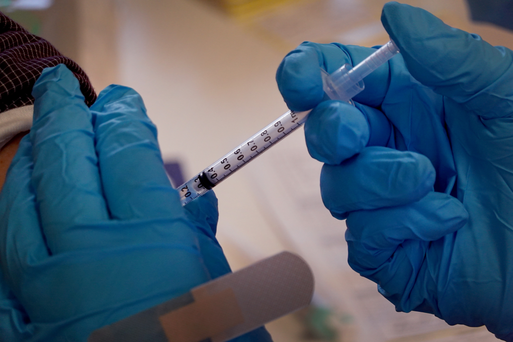 A close up of hands wearing blue surgical gloves, administering a vaccine.