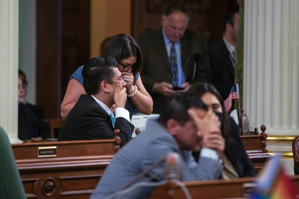 Men and women in suits and dresses are seated at tables and cover their mouths with their hands.