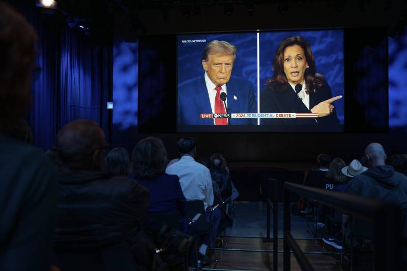 Several people are sitting facing a split screen showing a man and a woman.