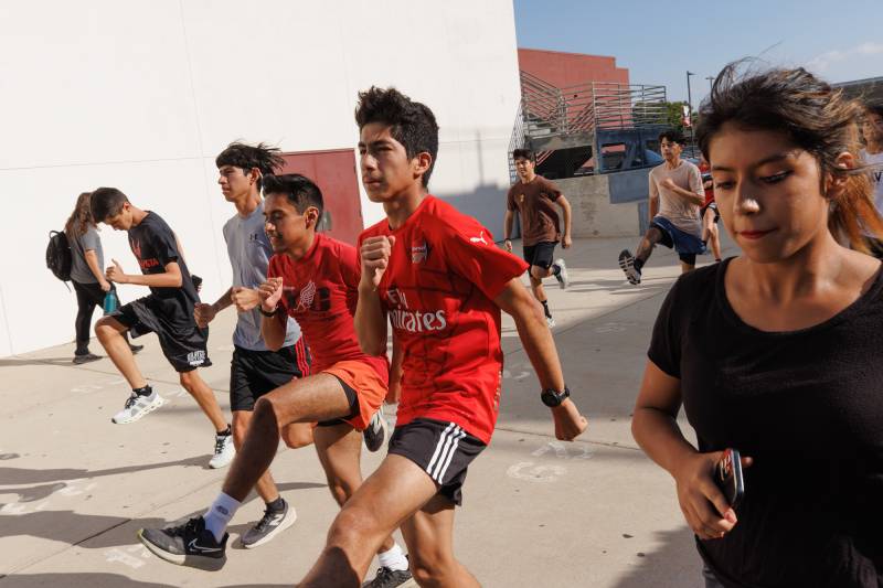 Young people wearing red, black and gray shirts stretch outside.