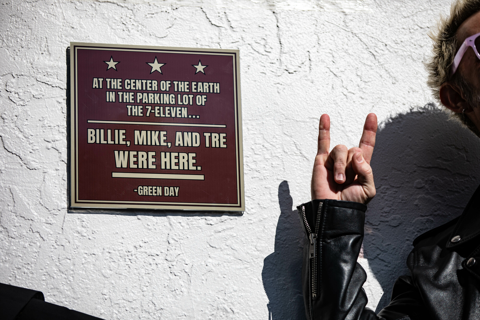 Next to a memorial plaque, someone makes a punk rock gesture with his hand.