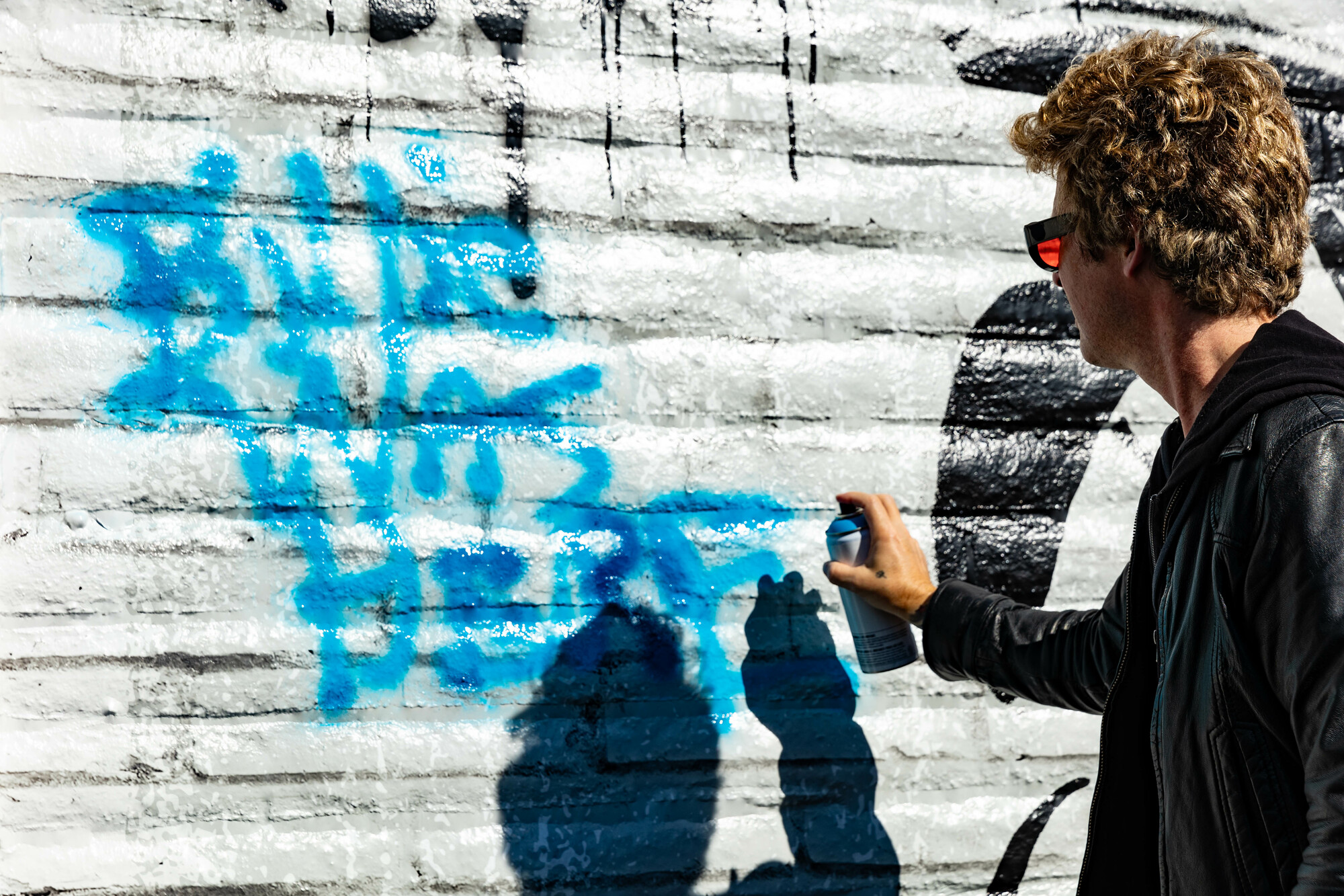 A man wearing sunglasses sprays paint on a wall.