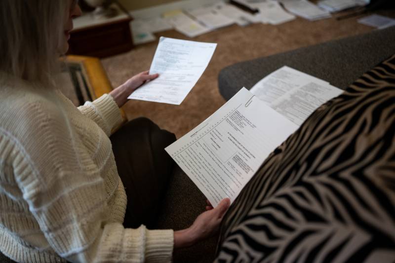 The hands of a seated woman, holding paperwork.