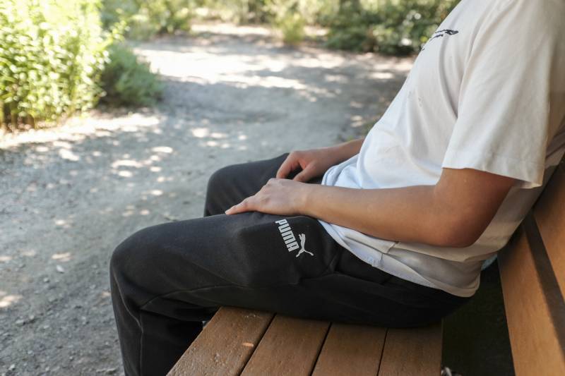 A young man sits on a bench outside.