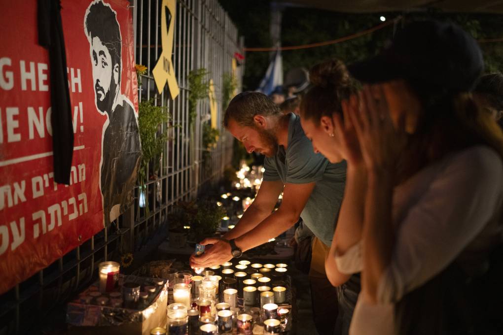 Several people stand in front of candles and an illustration as a man bends over to light a candle at night.