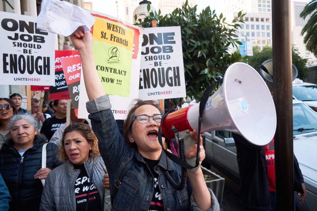 A person yells into a megaphone standing in front of protest signs.