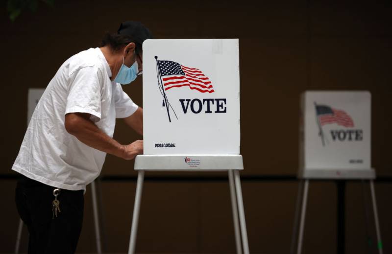 A man wearing a mask votes at a voting booth.