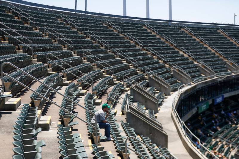 A man wearing a green and yellow cap sits alone in the upper deck seats of a stadium.