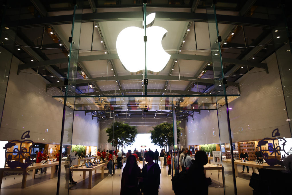 A large white apple logo is seen above a store as people walk in and out.