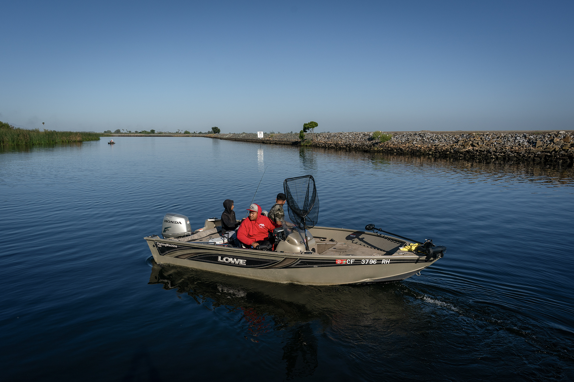 Three people sitting on a fishing boat in the middle of a body of water.