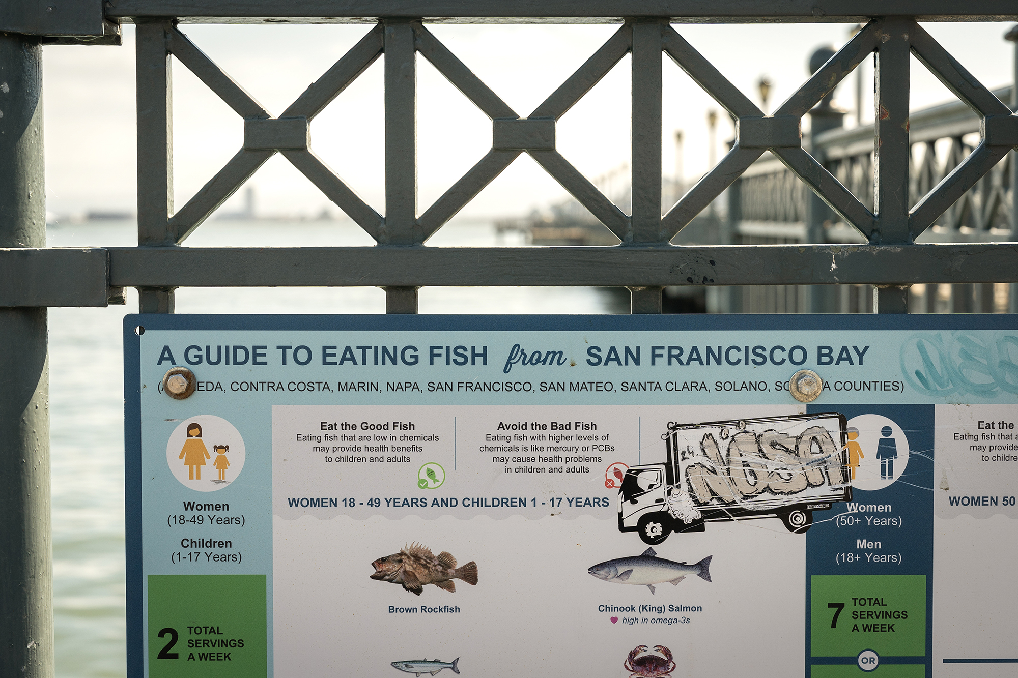 A sign with illustrations of fish and a truck with graffiti with text that reads "A Guide to Eating Fish From San Francisco Bay."