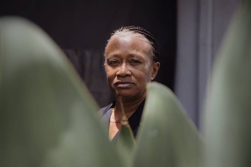 A closeup of a Black woman with plants in the foreground.