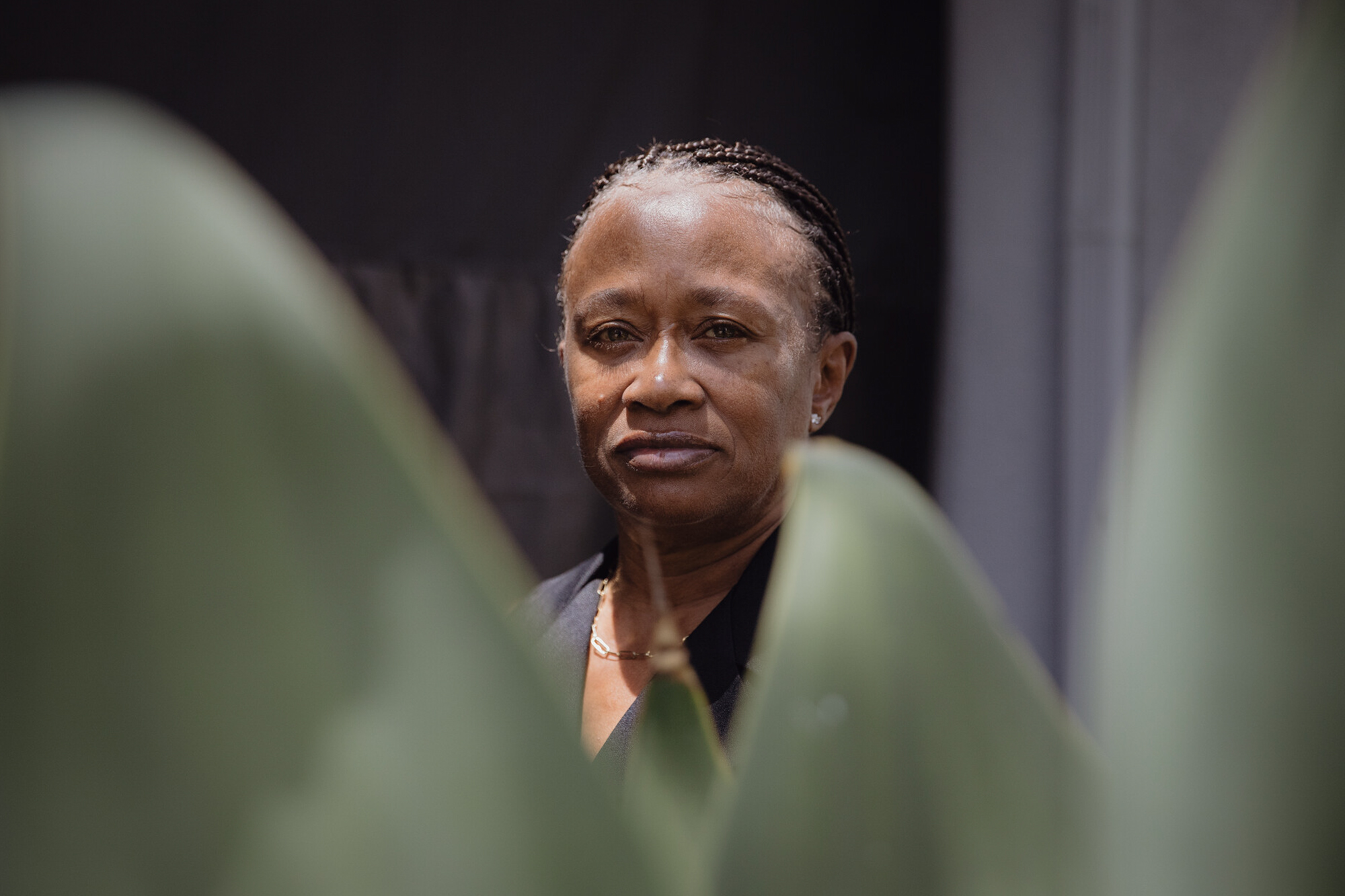 A closeup of a Black woman with plants in the foreground.