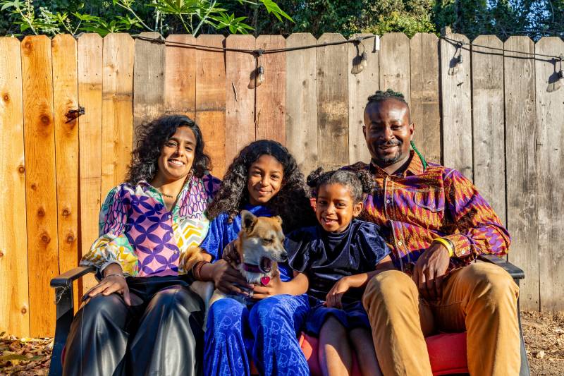 An Indian woman and a Black man sit on both sides of two young girls of mixed identities.