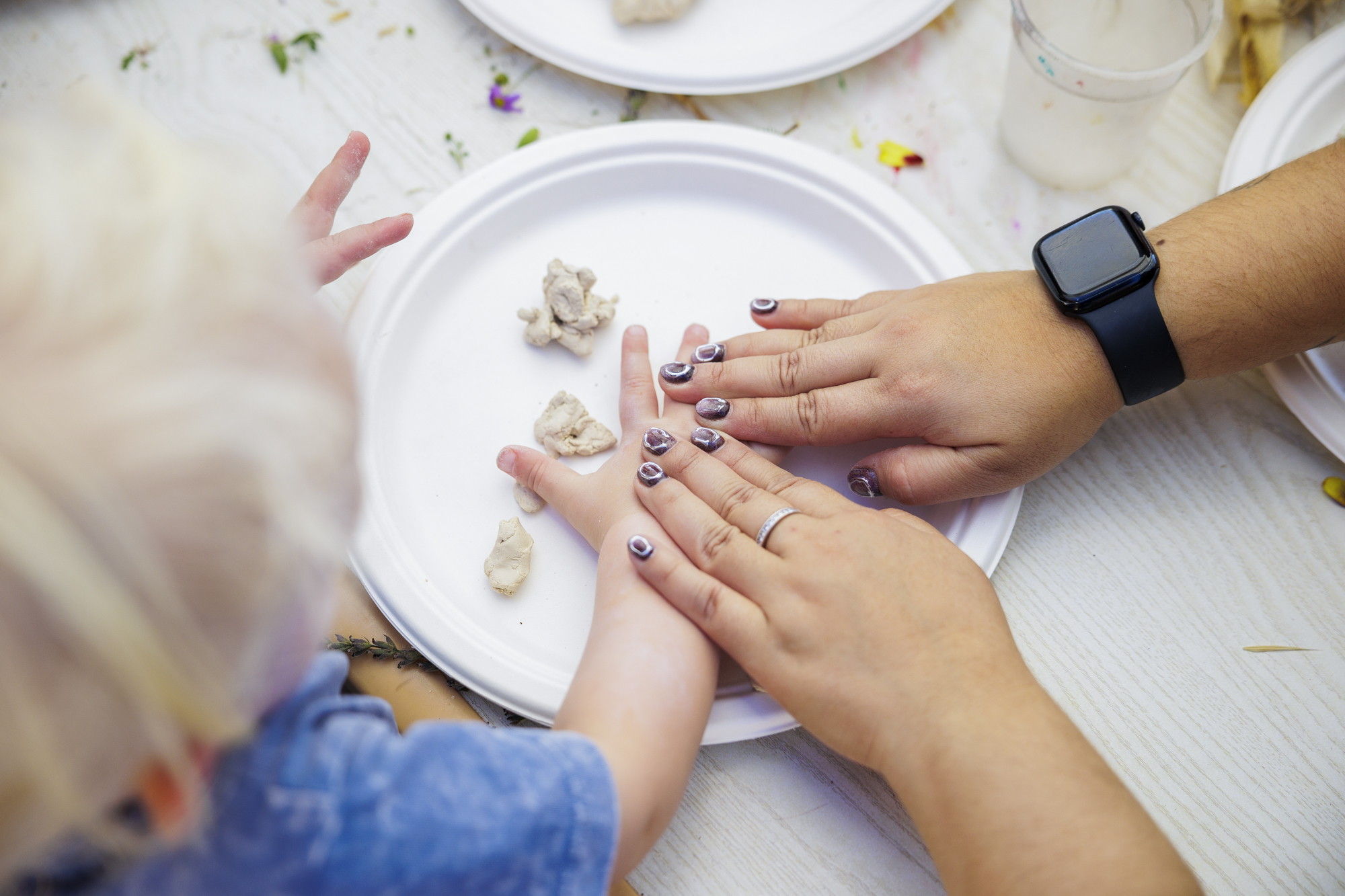 An adult's hands lay on top of a little kid's hands while making something with clay.