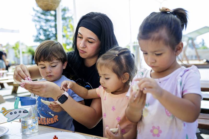 A young woman works with three young children at an activity table.