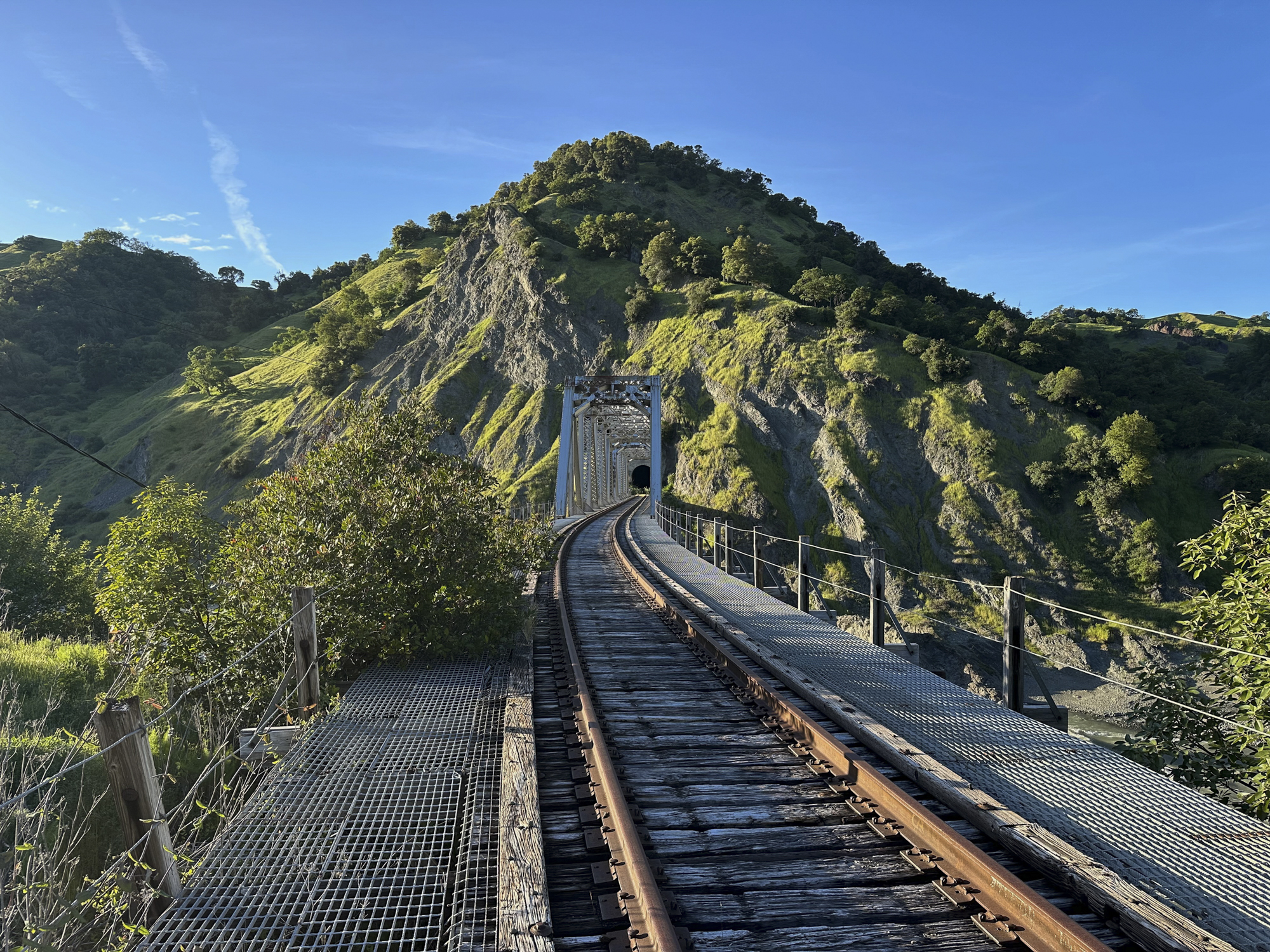 A view of a train bridge and tunnel going into a mountain.