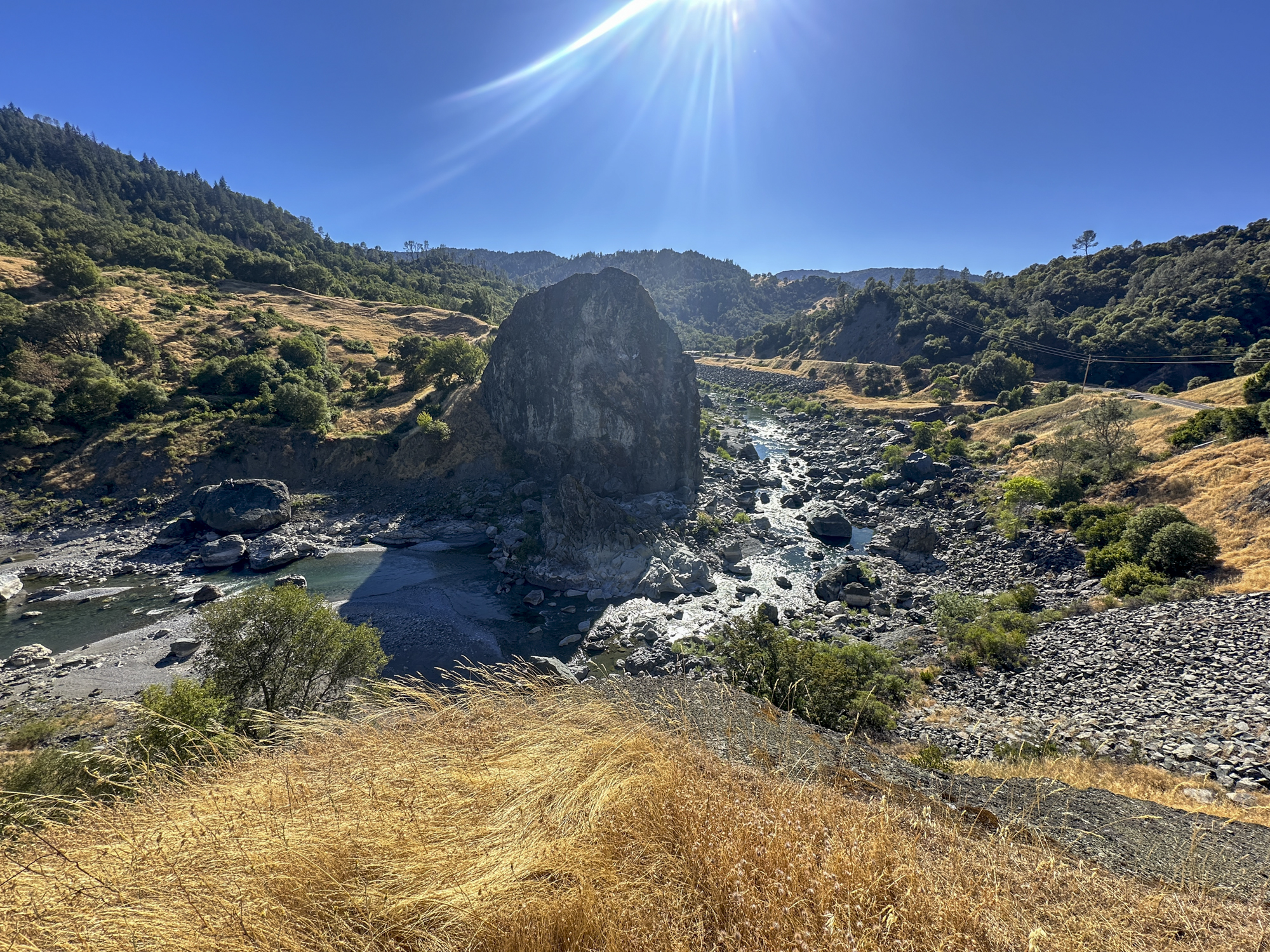 A view of a river with large rocks around the grassy landscape.