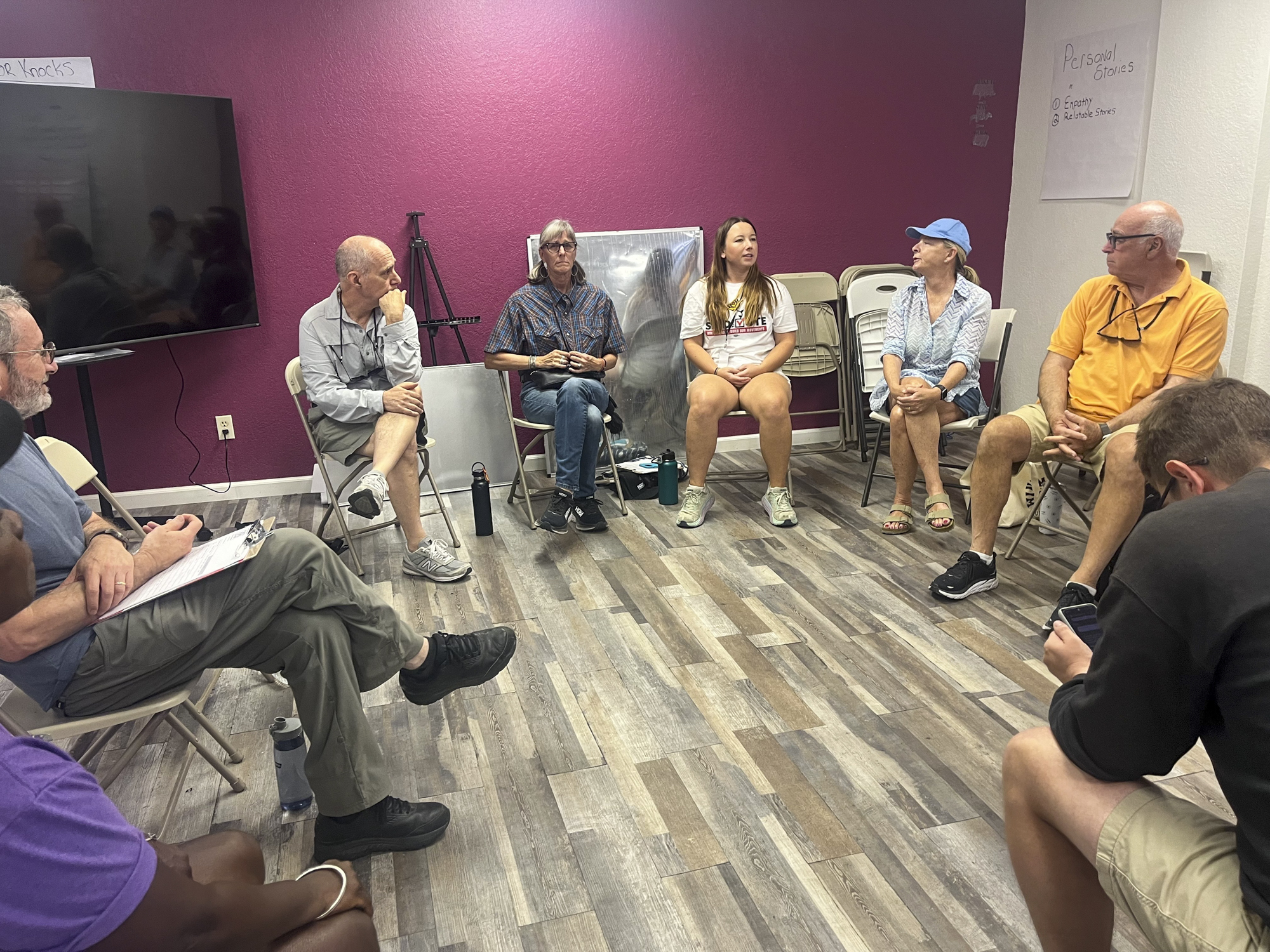 Eight people sit inside a room talking to each other.