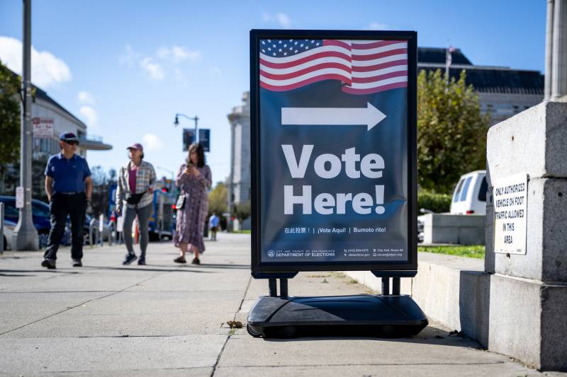 A sign says 'Vote Here!' with an arrow pointing to a polling place.