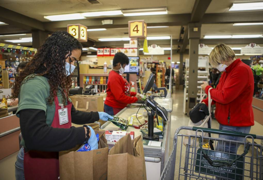 A bagger in a grocery store bags groceries as customers stand in line.