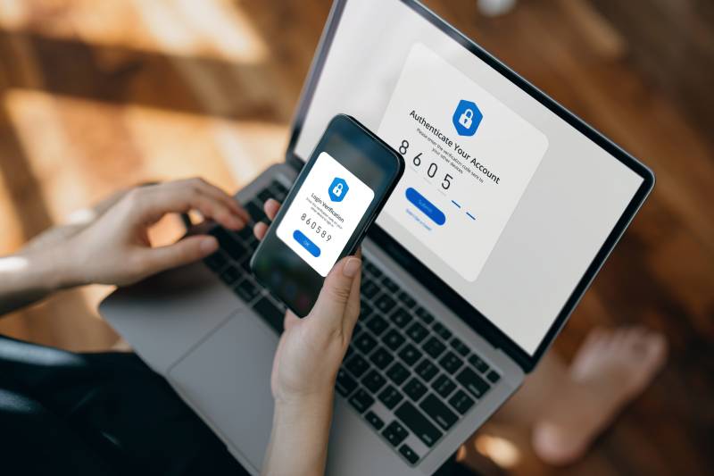 Cropped hand of a woman using a mobile device with Two-Factor Authentication (2FA) security while logging in securely to her laptop. Privacy protection, internet and mobile security.