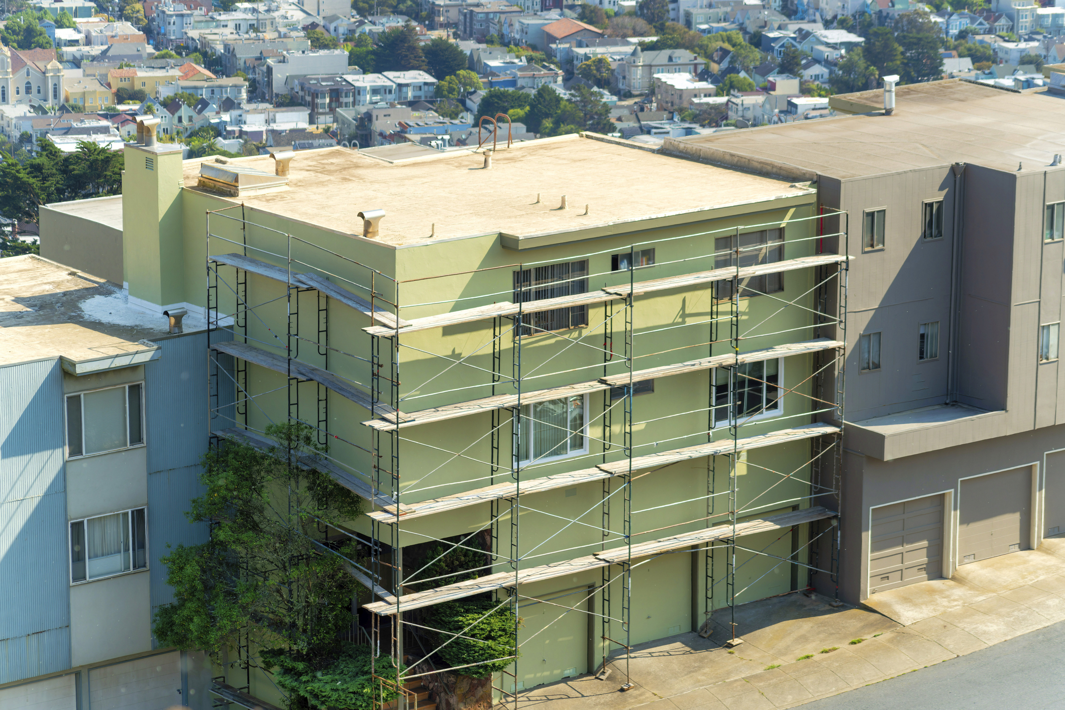 A row of multicolored houses with construction rafters in sun midday in a city aerial shot.