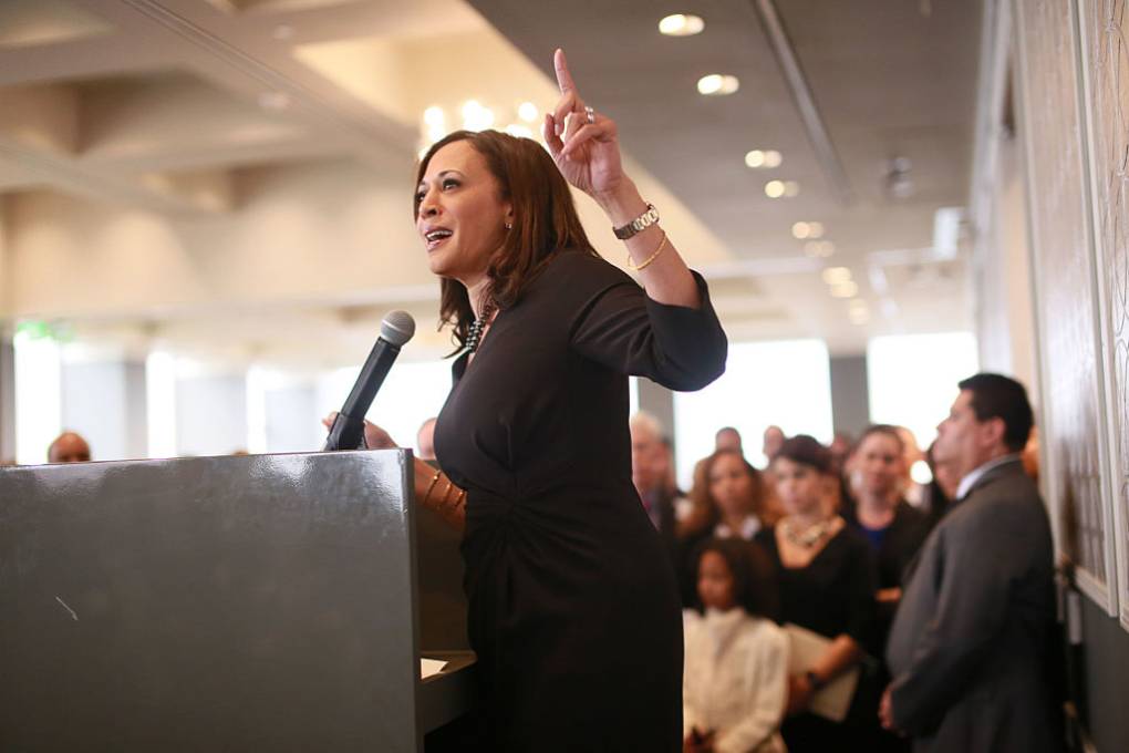 Kamala Harris stands at a lectern, delivering a speech with an audience behind her.