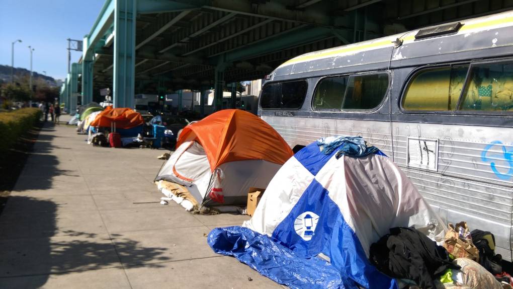 Tents with various items on a sidewalk next to a large vehicle.