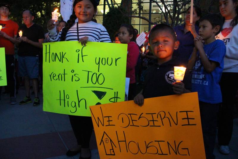 Two young people hold signs saying "honk if your rent is too high" and "we deserve housing" at a rally.