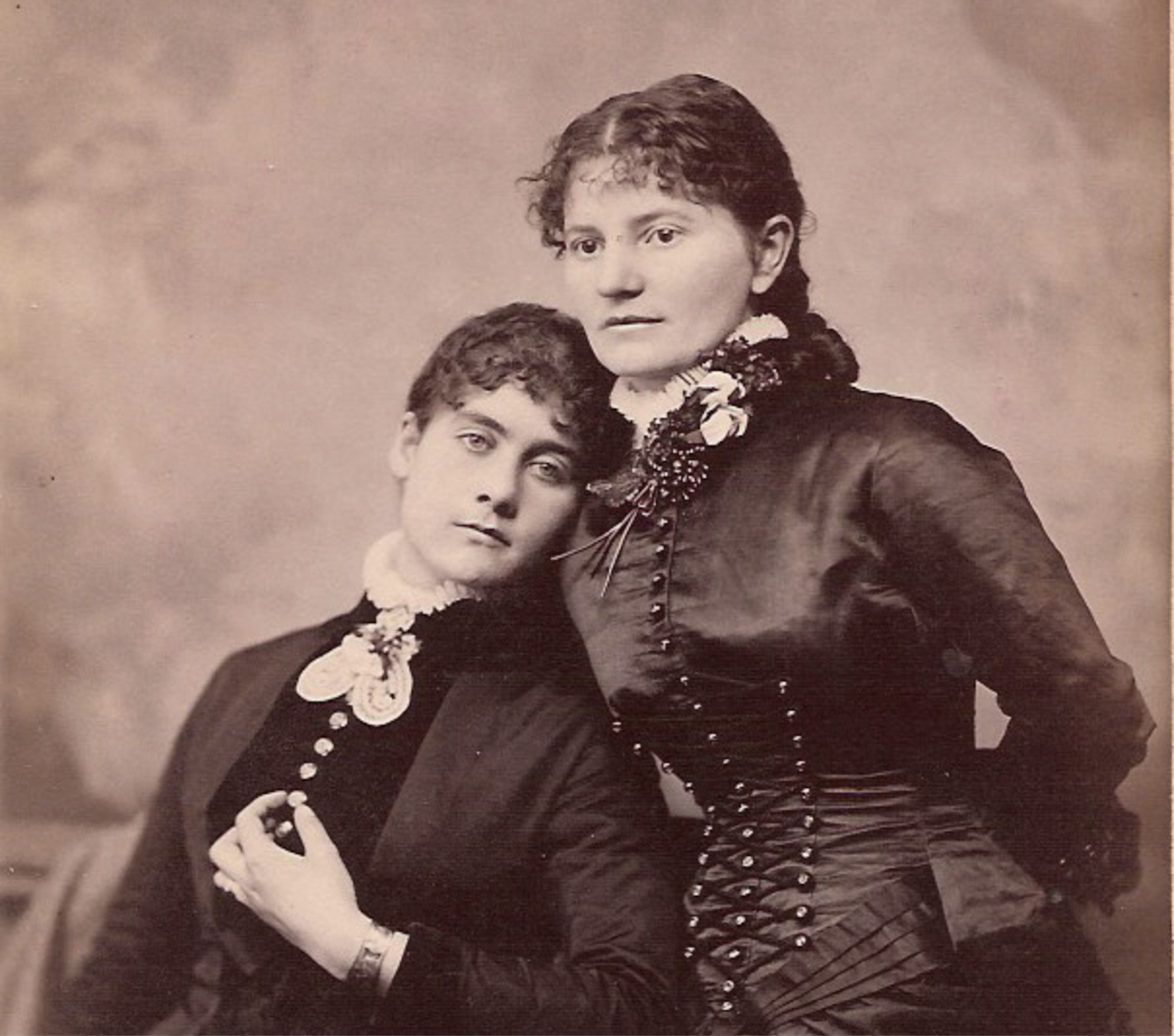 A vintage image of two women in dresses seated next to each other.