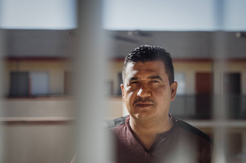 A man looks at the camera with light on his face and a house in the background.