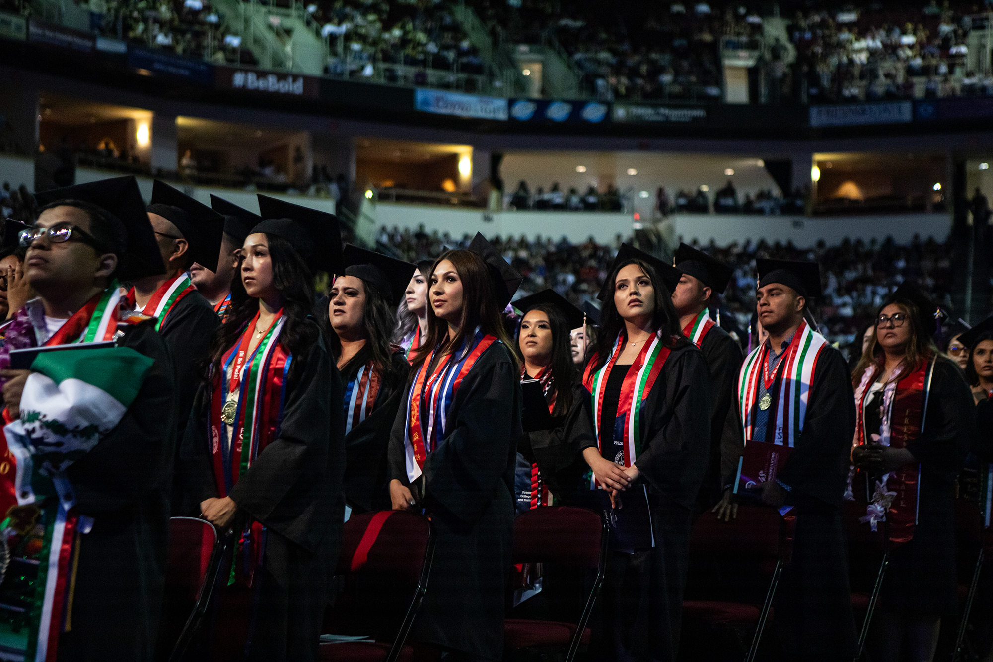 A large group of people dressed in black graduation caps and gown standing up inside a large building.