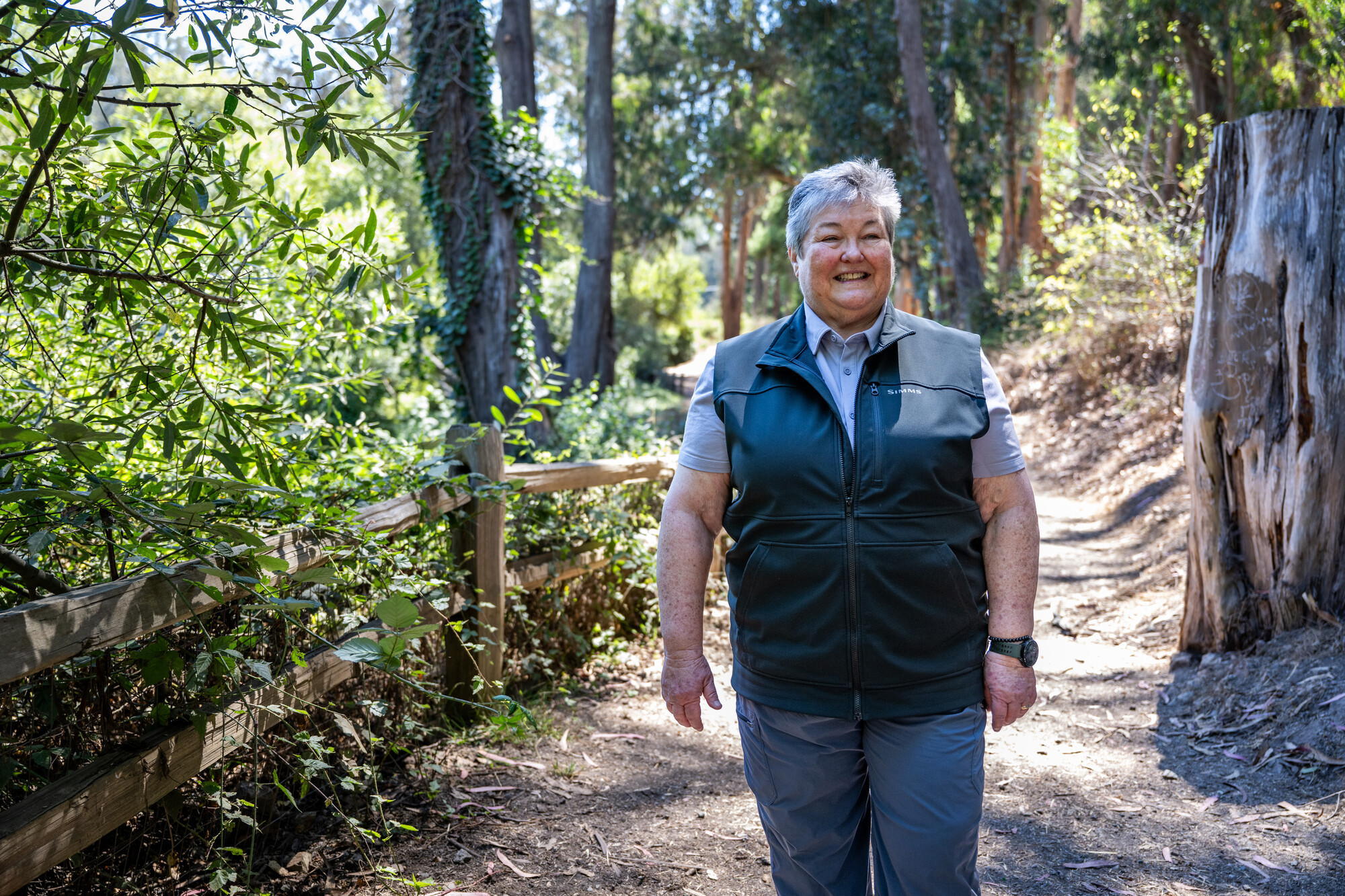 A person with short hair stands in a shaded park.