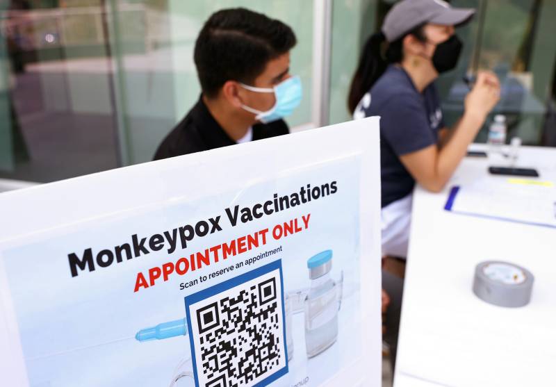 A sign saying monkeypox vaccinations appointment only with two people with masks in the background.