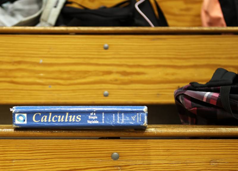 A blue textbook that says "Calculus" next to a bag on bleacher steps.