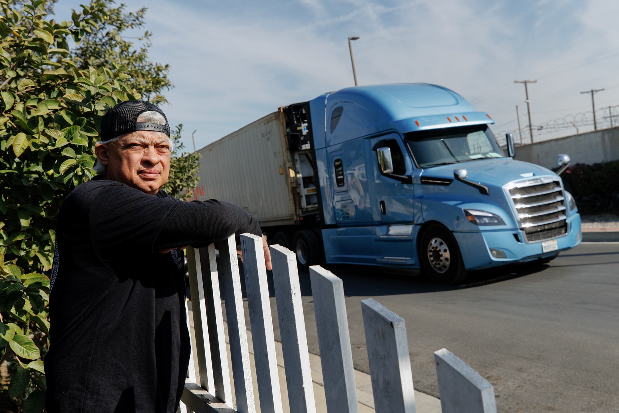 A man in a hat looks in the distance with a large blue truck in the background.