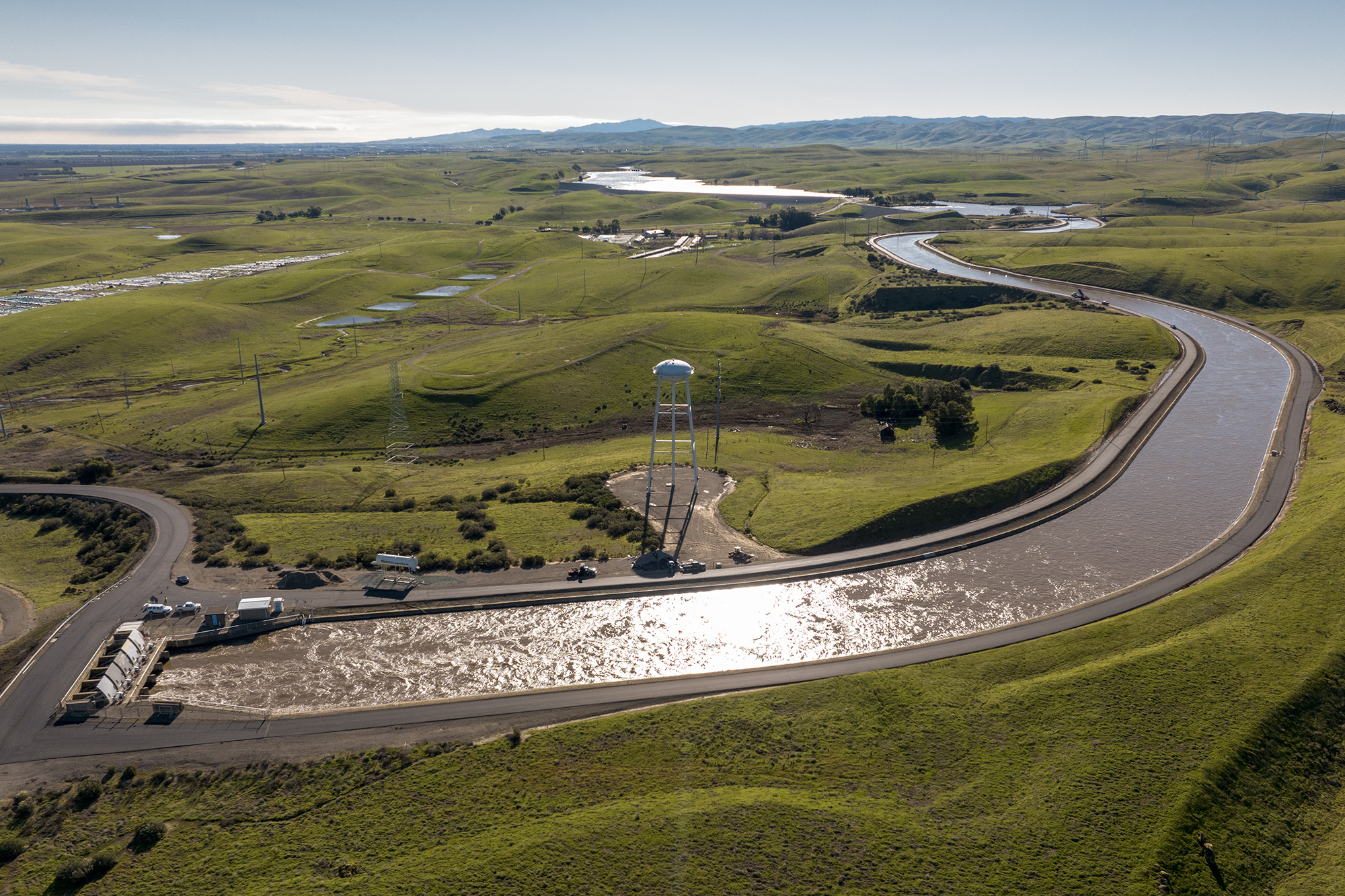 A wide drone shot from above an aqueduct with green grass and a water tower.