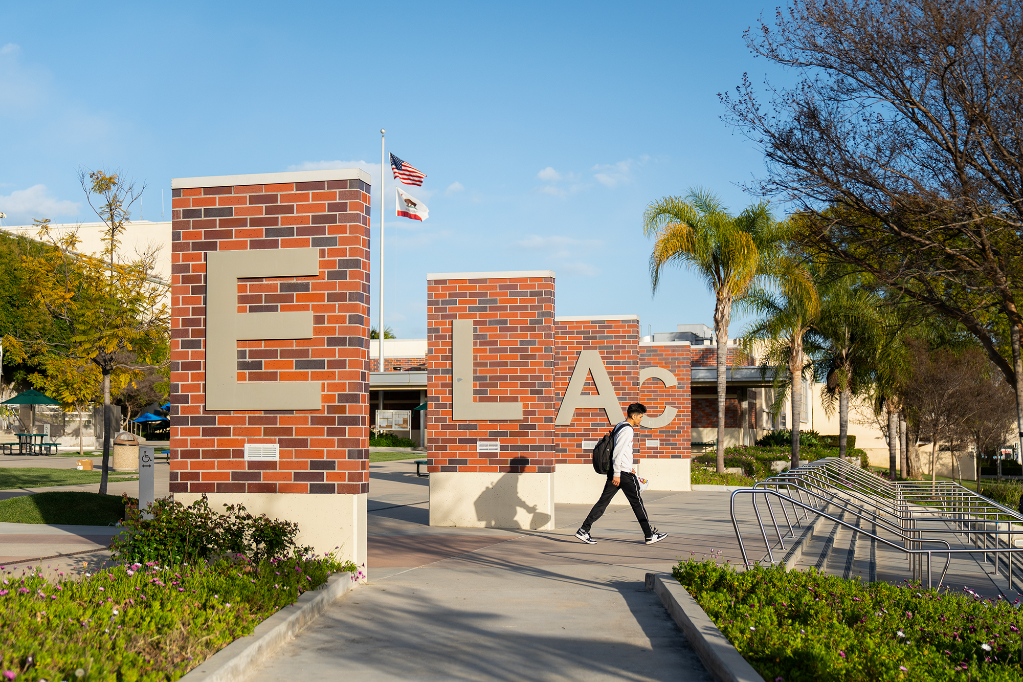 A student walks next to campus buildings with the letters "E" "L" "A" and "C"