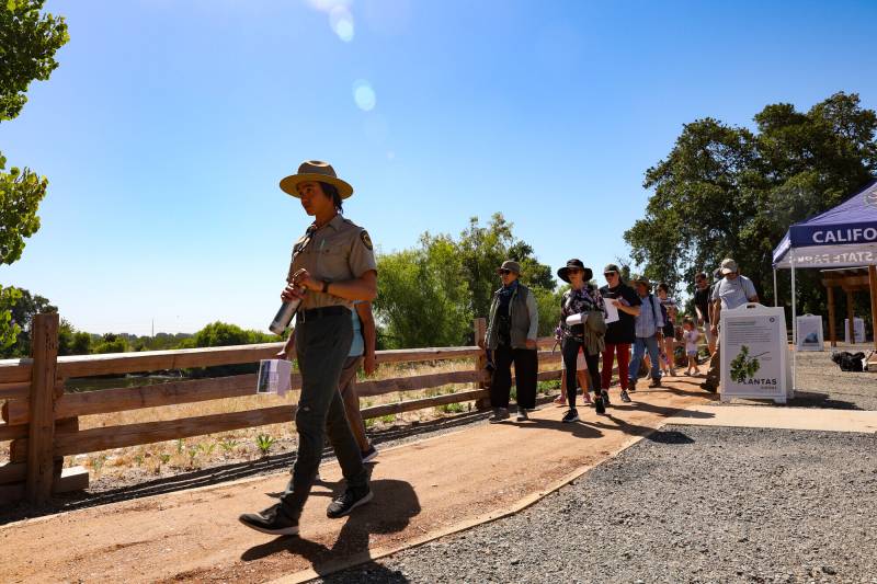 A person in a hat walks ahead of several others with a background of blue sky.