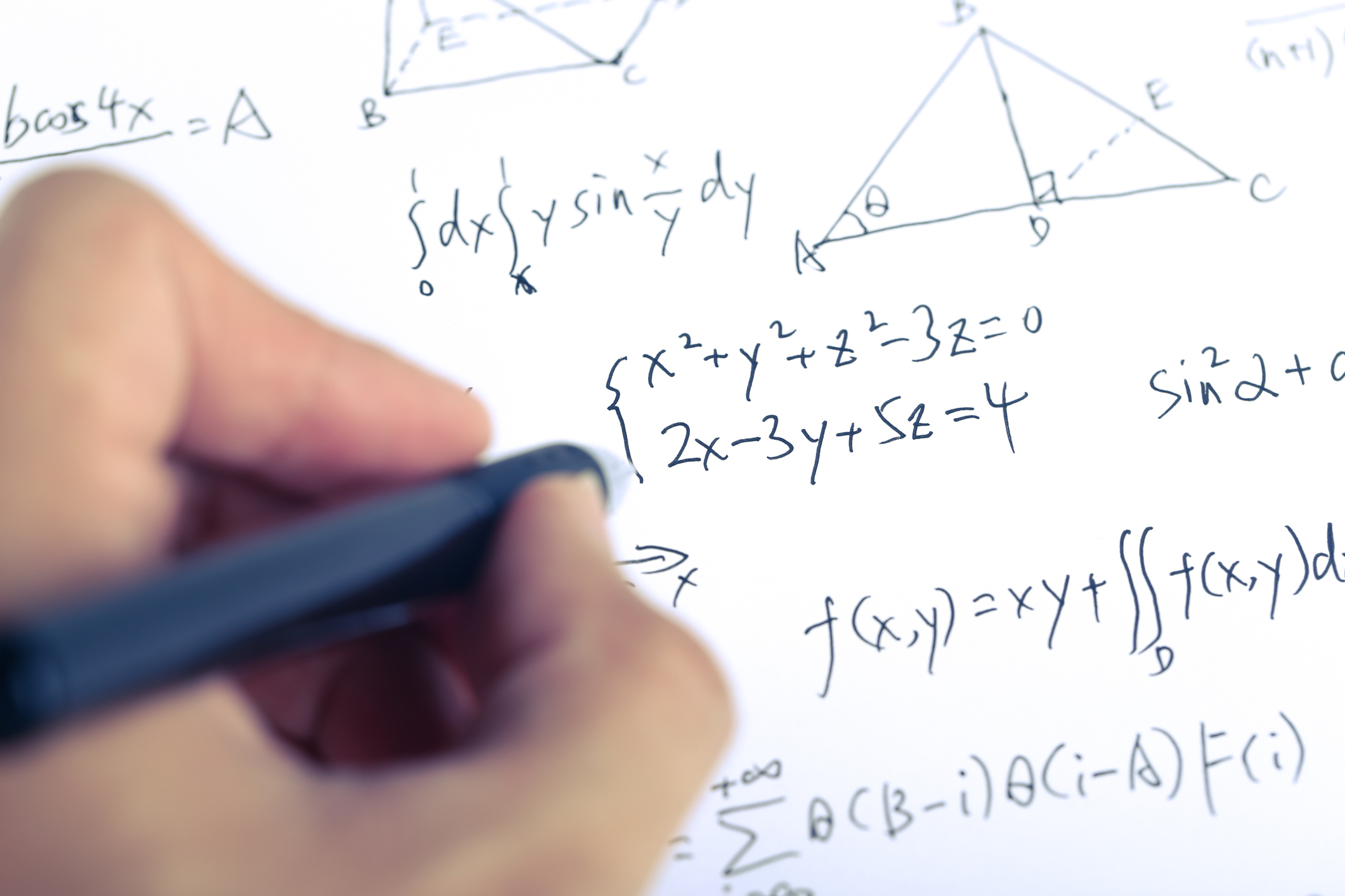 A closeup shot of complex math formulas on paper with a hand holding a ball pen.