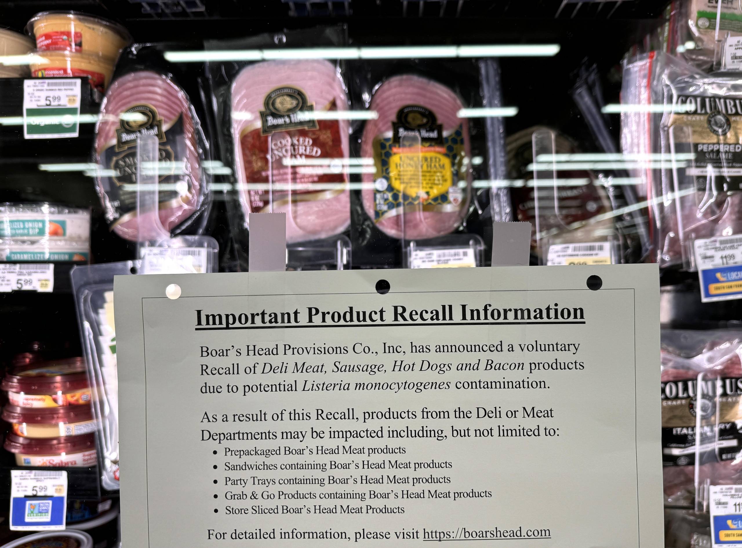A food recall notice posted in a store next to a refrigerated meats.