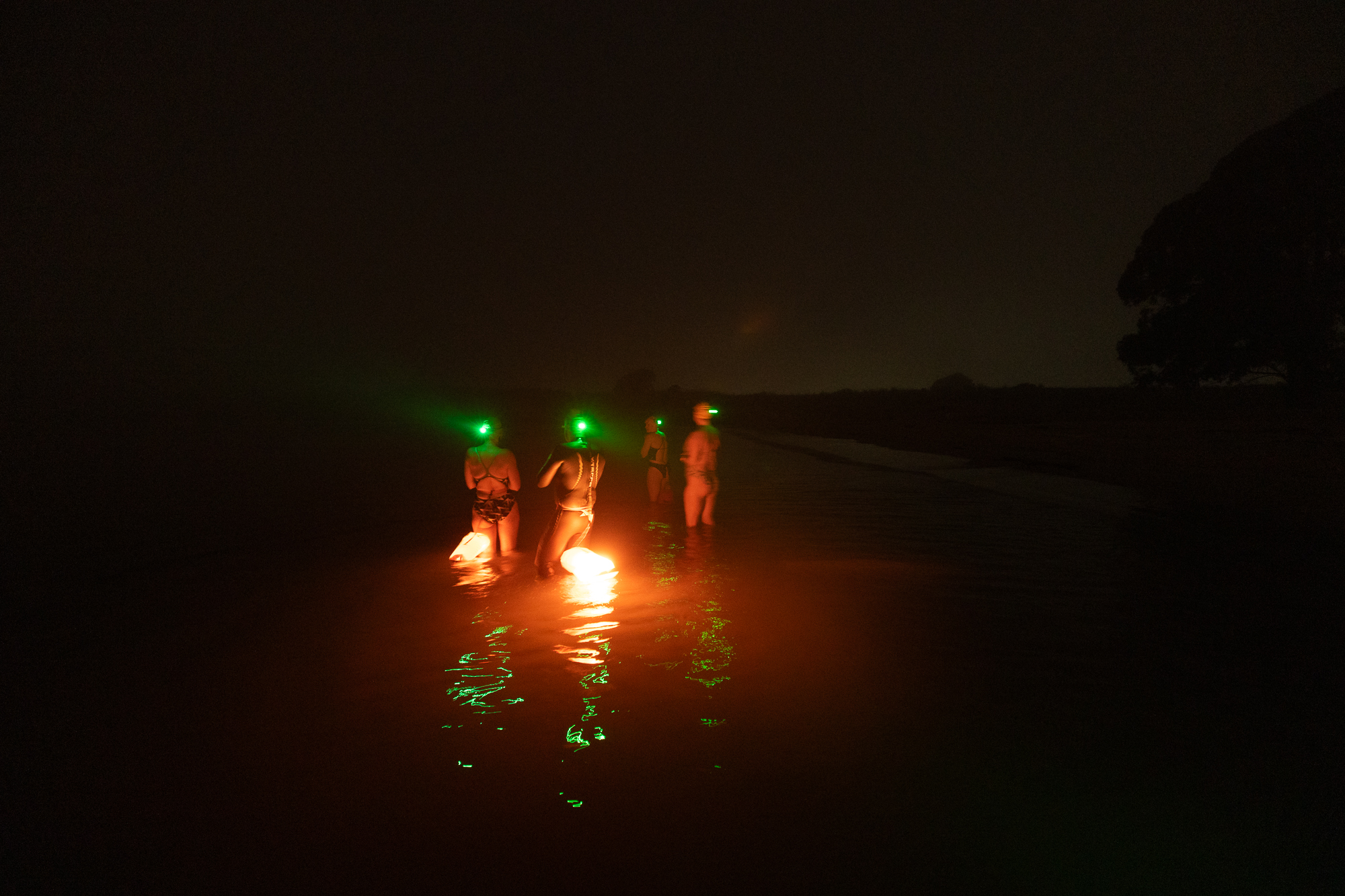 Three people with lanterns stand in a body of dark water.