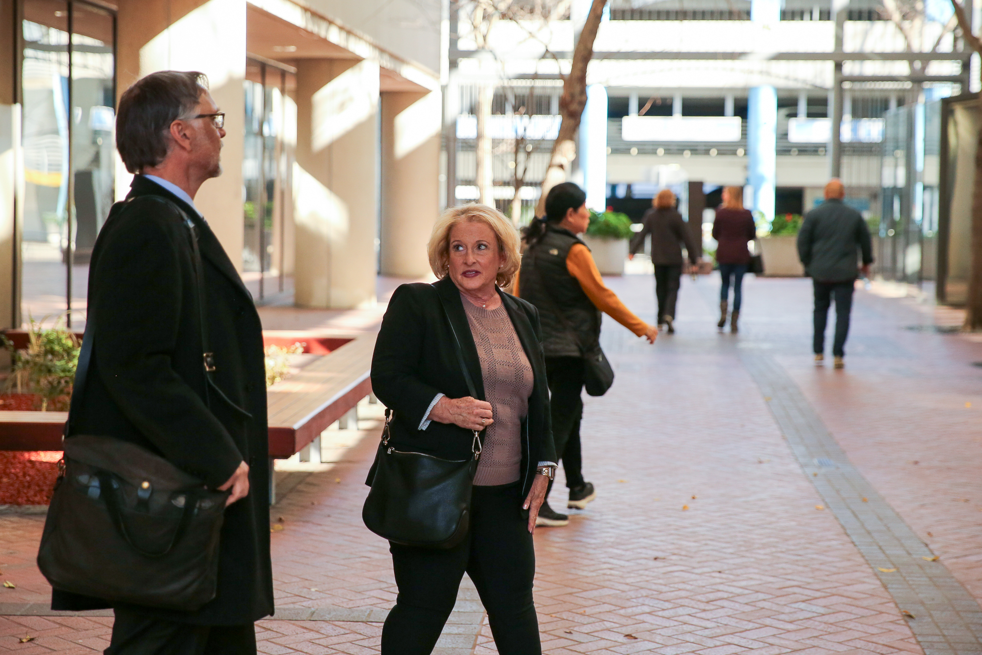 A middle-aged woman walks out of a court building next to a man holding a briefcase.