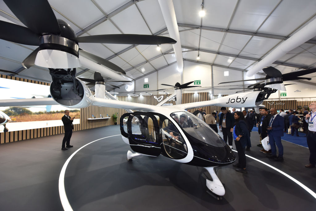 An electric aviation vehicle with sets of propellers and a cabin sits in a showroom at a fair.