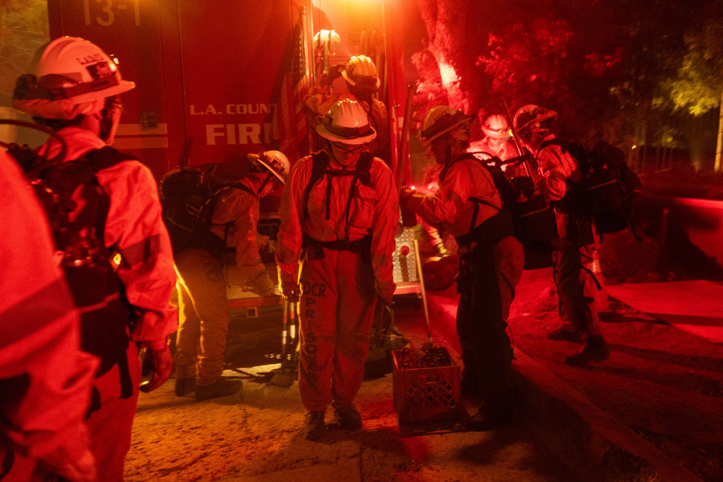 Firefighters prepare beside a firetruck amid a red, hazy glow.