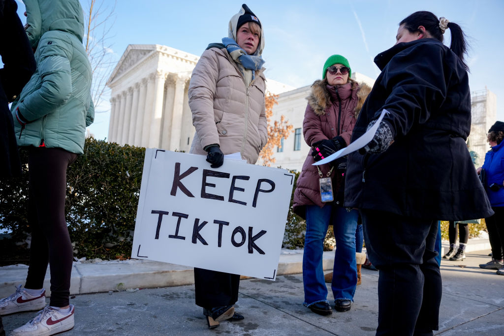 Three women stand outside a neo-classical white building with coats, scarves and beanies, one of them holding a sign that reads 'Keep TikTok.'