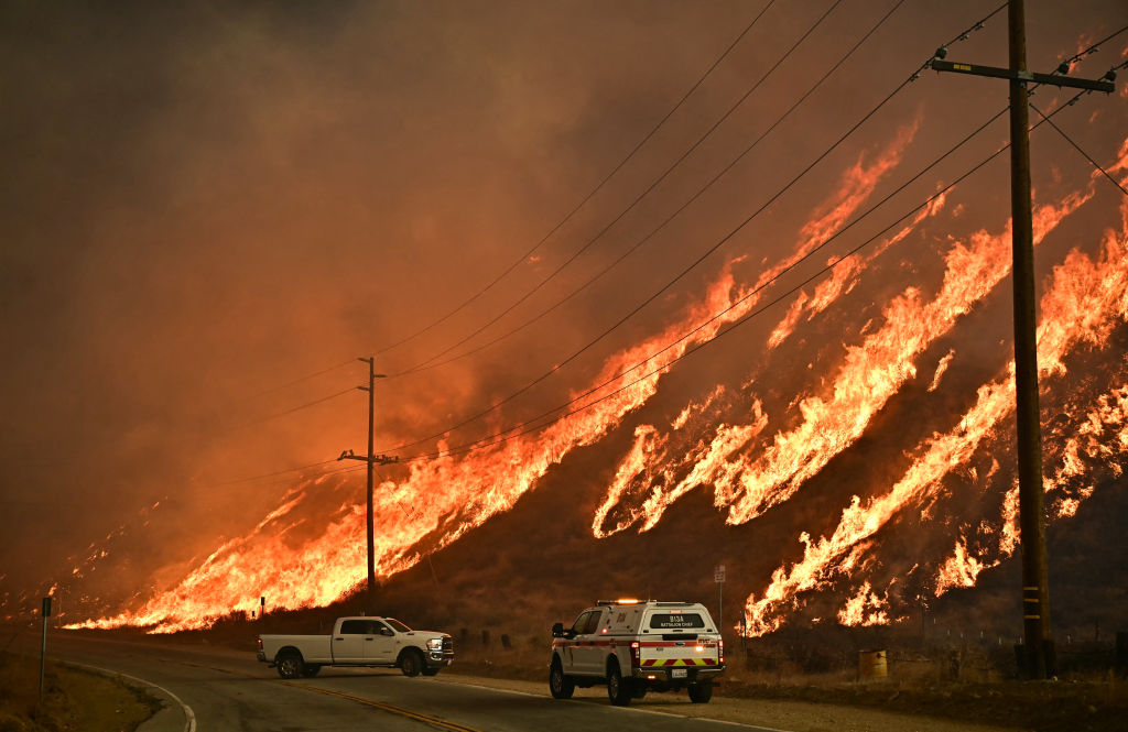 A hillside on fire, with fire trucks on the road.